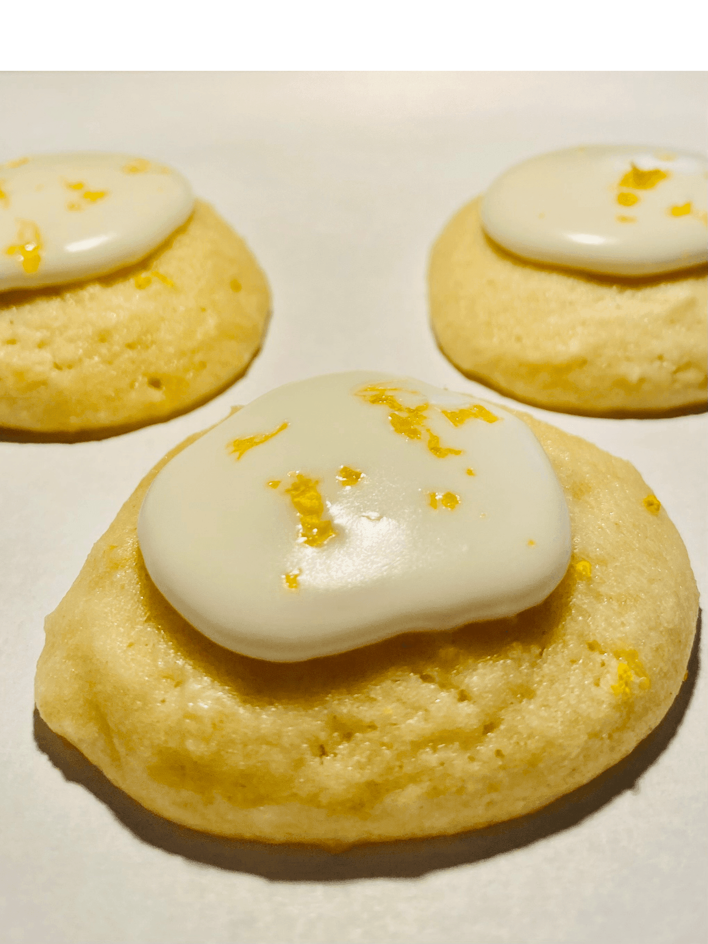 Three lemon cookies with glaze and orange zest on a white surface.