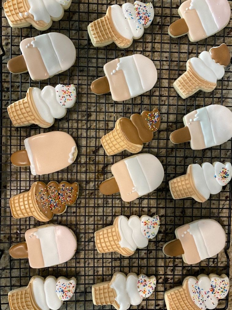 Decorated cookies shaped like ice cream cones and popsicles on a cooling rack.