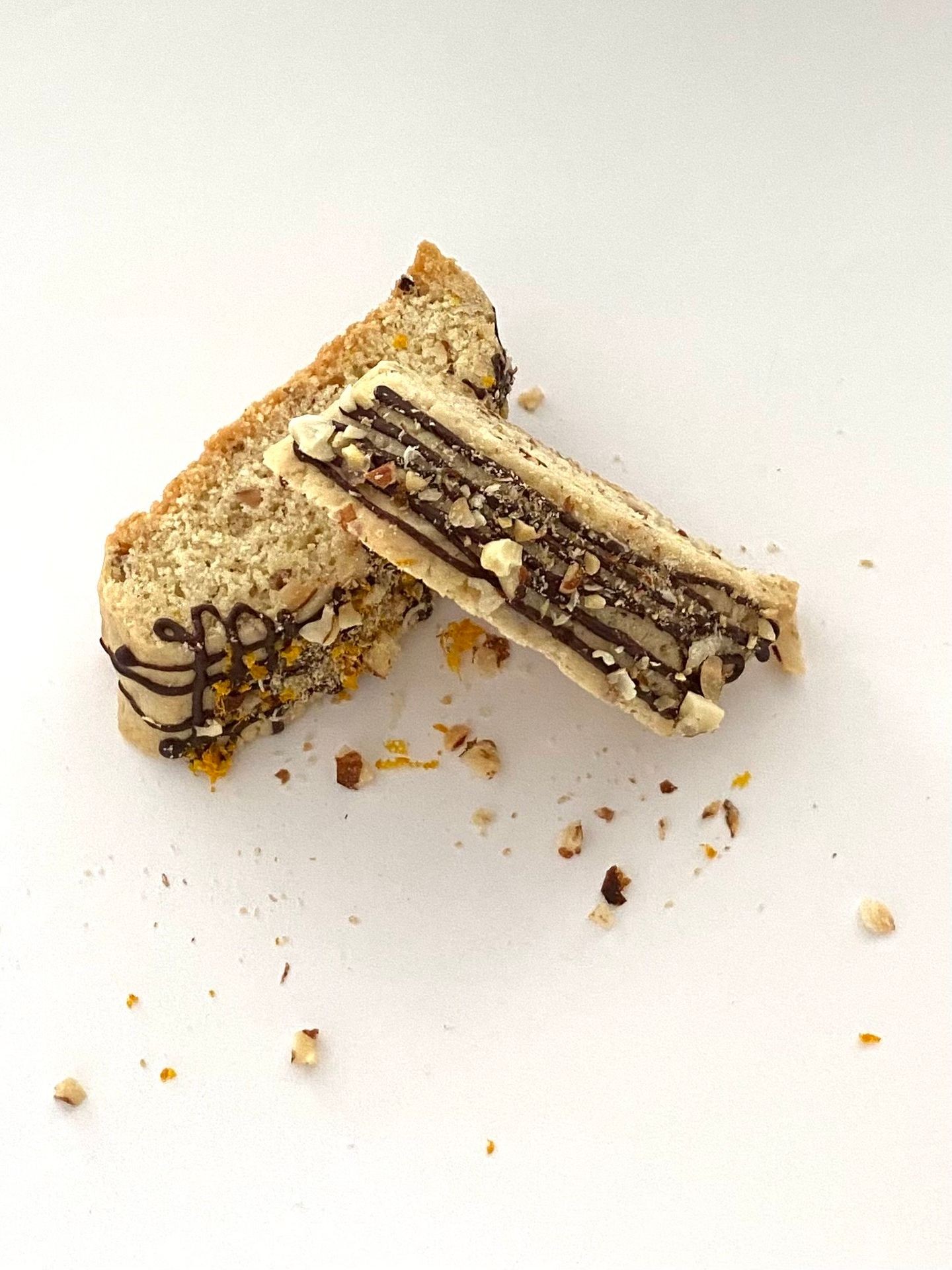 Two sliced pieces of biscotti with chocolate drizzle and chopped nuts on a white background.