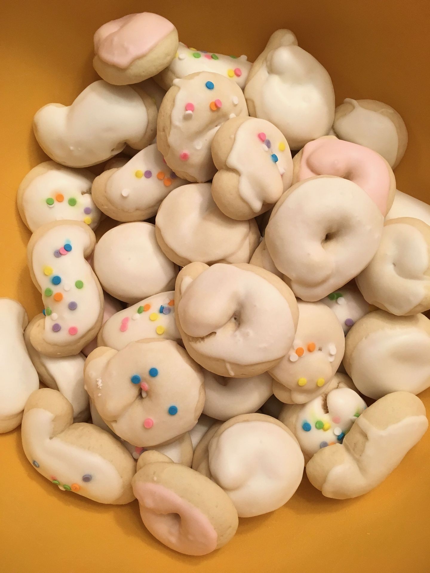 Bowl of Italian cookies with white icing and colorful sprinkles in a yellow bowl.