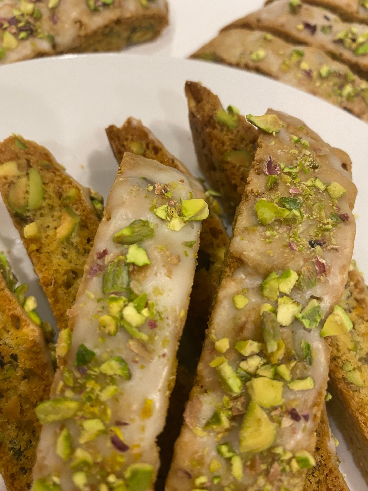 Close-up of pistachio biscotti slices topped with icing, arranged on a white plate.